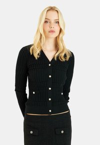 Schwarze gerippte Strickjacke mit V-Ausschnitt, langen Ärmeln, Perlenknöpfen und zwei Taschenakzenten. Strukturiertes Strickmaterial, taillierte Passform.