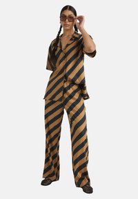 Striped to-delt sett i brun og svart; kortermet, knappet skjorte og løse bukser med en glatt tekstur.