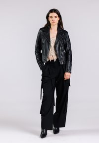 Chaqueta de biker de cuero negro con cremallera en el frente, top de crochet crema, pantalones cargo negros con bolsillos y lazos, combinados con botas negras hasta el tobillo.