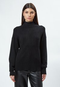 Schwarzer gestrickter Pullover mit hohem Kragen und aufwendigem Texturmuster. Er hat lange Ärmel und einen gerippten Saum und besteht aus weichem Material.