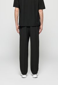 Zwart kort mouwtshirt met een geribbelde textuur, gecombineerd met zwarte, loszittende broek. Witte sneakers maken de outfit compleet.