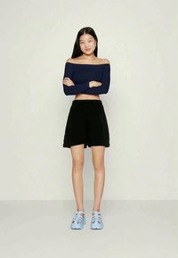 Blusa azul escura de ombros à mostra, calções pretos e sandálias azul claro. A blusa é justa, enquanto os calções têm uma cintura elástica e um corte descontraído.