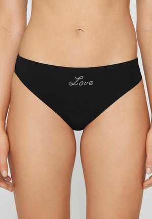 Žena v černých spodních dílech bikiny s nápisem "Love" z hotových kamenů uprostřed předního pásku.