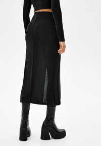 Falda midi negra ajustada con una abertura lateral, hecha de un tejido liso. Combinada con botas de plataforma negras hasta la rodilla.