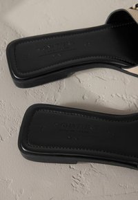 Svarta slidesandaler med en slät lädersula, med en platt design och präglad branding. Utsmyckad med ett något texturerat övre rem.