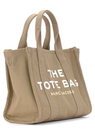 Bolso de lona beige con dos asas cortas, con el texto en blanco "THE TOTE BAG" y "MARC JACOBS" en la parte frontal, diseño estructurado.