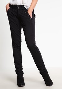 Svarta slim fit-jeans med dekorativ sömnad på fickorna, som har två knappar i midjan och en smal, avsmalnande design.