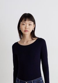 Langslijze, aangenaam zittende bodysuit van zwarte stof, met een brede halslijn en een soepele textuur, gecombineerd met hoge spijkerbroek in blauw.