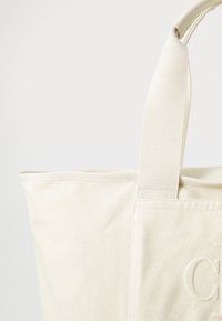 Canvas tote bag i off-white, med robustt stoff, forsterkede håndtak og preget detaljer på forsiden. Enkel og funksjonell design.