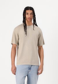 Beige kortærmet t-shirt med afslappet pasform, lavet af blødt stof med rund hals og subtil tekstur, parret med lyseblå jeans.