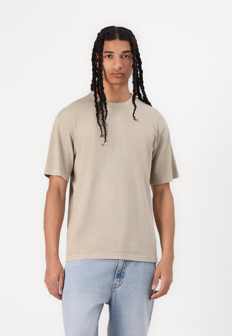 Beige kortærmet t-shirt med afslappet pasform, lavet af blødt stof med rund hals og subtil tekstur, parret med lyseblå jeans.