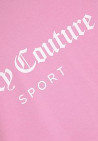 T-shirt rose avec un grand texte blanc qui indique "Couture SPORT." Fabriqué en tissu doux avec une texture lisse.