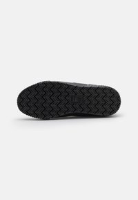 Semelle extérieure noire de chaussure de sport avec un motif de grip texturé. La semelle présente des motifs en chevrons pour assurer adhérence et durabilité.