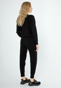 Schwarzer Strickpullover und passende Jogginghose, mit lockerer Passform, gerippten Bündchen und Saum, kombiniert mit klobigen schwarzen Sneakers mit goldenen Akzenten.