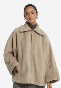 Beige, överdimensionerad fleecejacka med krage och dragkedjeslutning. Har vida ärmar och sidofickor, vilket erbjuder en mjuk, texturerad finish.