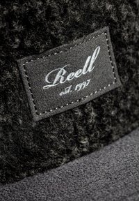 Schwarze Wollmütze mit strukturiertem Finish, versehen mit einem grauen Stoffpatch, der "Reell" und "est. 1997" in weißer Schrift zeigt.