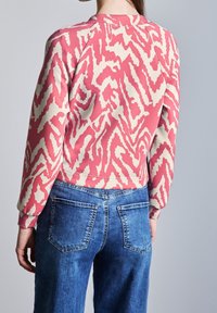 Rosa bomullströja med krämfärgad zigzagmönster, ribbade ärmslut och rund halsringning, tillsammans med vida jeans i blå denim med bakfickor.