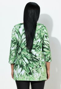 Zielona bluzka w kwiatowy wzór z rękawami o długości za łokieć, charakteryzująca się luźnym krojem i lekkim materiałem. Dopasowana do czarnych spodni.