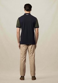 Námornícky polo tričko so zelenými krátkymi rukávmi, z bavlneného zmesi, s predným golierom, nosené s béžovými nohavicami a hnedými topánkami, pohľad zozadu.