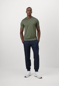 Olivegrønn T-skjorte med en subtil logo, kombinert med marineblå joggebukser. Begge plaggene har en jevn tekstur, designet for komfort. Hvite joggesko.