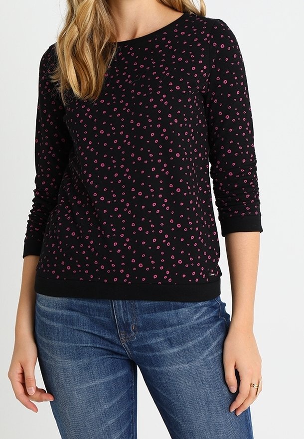 Maglietta nera a maniche lunghe con scollo rotondo, caratterizzata da un motivo floreale rosa e una cintura nera uniforme. Abbinata a jeans blu.