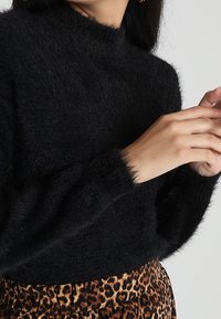 Svart, fluffig polotröja med långa ärmar, kombinerad med en leopardmönstrad kjol som har en mjuk textur och avslappnad passform.