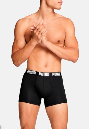 Schwarze Baumwoll-Boxershorts mit einem elastischen Bund, auf dem das "PUMA"-Logo in Weiß zu sehen ist. Die Passform ist enganliegend mit einer Länge bis zur Mitte des Oberschenkels.