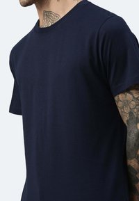 T-shirt blu navy a maniche corte realizzato in tessuto morbido, con colletto classico a girocollo. Vista ravvicinata che mette in evidenza la texture liscia e la vestibilità.