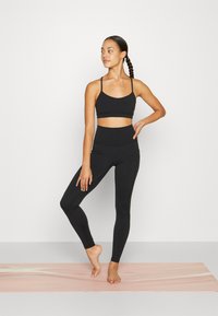 Zwarte sportieve crop top met dunne bandjes, gecombineerd met hoge zwarte leggings. De stof lijkt rekbaar en soepel te zijn.