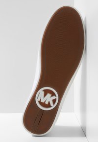 Suela de zapato con agarre texturizado marrón y un logo circular blanco con las letras "MK" sobre un fondo blanco.