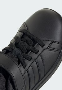 Czarny but sportowy z syntetyczną skórzaną cholewką, płaskie czarne sznurowadła i wyściełany kołnierz. Posiada teksturowane akcenty oraz boczne paski.