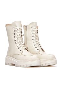 Bottes de combat en cuir blanc avec finition texturée, dotées de lacets, d'une fermeture éclair sur le côté et d'une semelle en caoutchouc épaisse avec des motifs de bande de roulement bien définis.