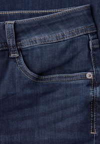 Zbliżenie na granatowe dżinsy, ukazujące przednią kieszeń, szlufkę na pasek, podwójne szwy oraz metalowy nit.