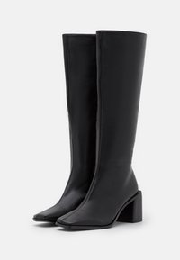 Czarno skórzane botki do kolan o gładkiej teksturze, kwadratowym nosku i masywnym obcasie. Czyste linie i solidna konstrukcja.