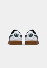 Puma-sneakers i hvit og teal med såle av gummi. Har en polstret krage, mesh-detaljer, og en logo på hælen.