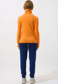 Oranger Rollkragenpullover kombiniert mit dunkelblauen Hosen, aus weichen Materialien gefertigt, mit einer schlanken Passform und gerippten Bündchen.