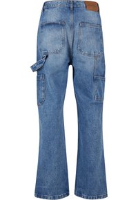 Mėlyni džinsai iš džinso medžiagos su platėjančiomis kojomis, su rudos odos pledu, dviem galinėmis kišenėmis ir šonine karinių cargo tipo kišene su dirželio detalėmis.