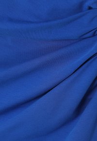 Tissu bleu lisse avec des plis doux et une texture subtile, drapé pour créer des courbes et des ombres délicates.