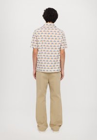 Kurzarmhemd in Weiß mit bunten Mustern, kombiniert mit beigen, lockeren Hosen. Das Hemd hat einen normalen Kragen und einen geraden Schnitt.