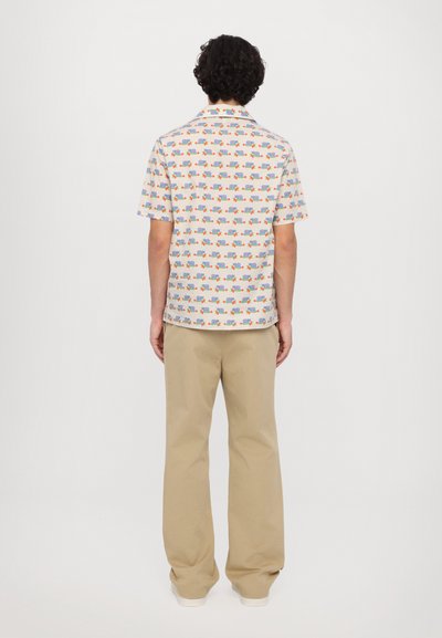 Chemise à manches courtes blanche avec des motifs colorés, associée à un pantalon beige ample. La chemise est dotée d'un col classique et d'une coupe droite.