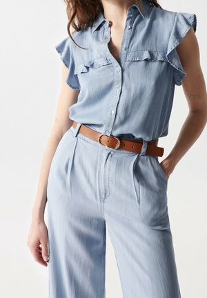 Light blue chambray shirt with ruffle sleeves, button-down front, paired with matching pleated trousers and a brown leather belt.