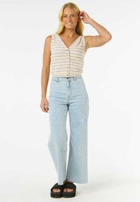 Haut sans manches de couleur claire avec des rayures verticales et des boutons ; associé à un jean bleu clair taille haute et à des sandales à plateforme noires.