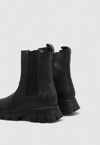 Botines negros de tobillo hechos de cuero texturizado, con paneles laterales elásticos, cierre de cremallera y suelas de goma gruesas con un diseño de banda de rodadura.