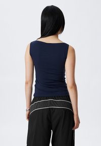 Top sans manches bleu marine avec un décolleté en forme de rond, fabriqué en tissu extensible et doux. Le dos est lisse et moulant, associé à un pantalon noir ample.
