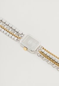 Ceas metalic cu carcasă rectangulară argintie, coroana aurie și brățară din lanț multiplu ce prezintă linkuri argintii și aurii. Design texturat și finisaj lustruit.