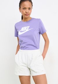 T-shirt en coton violet avec un logo Nike blanc, associé à un short gris clair. Le short est doté d'une taille élastique et de poches latérales.