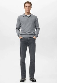 Suéter gris de punto con cuello de solapa, combinado con jeans de mezclilla gris oscuro. Usado con zapatos negros, mostrando un ajuste entallado y tela texturizada.