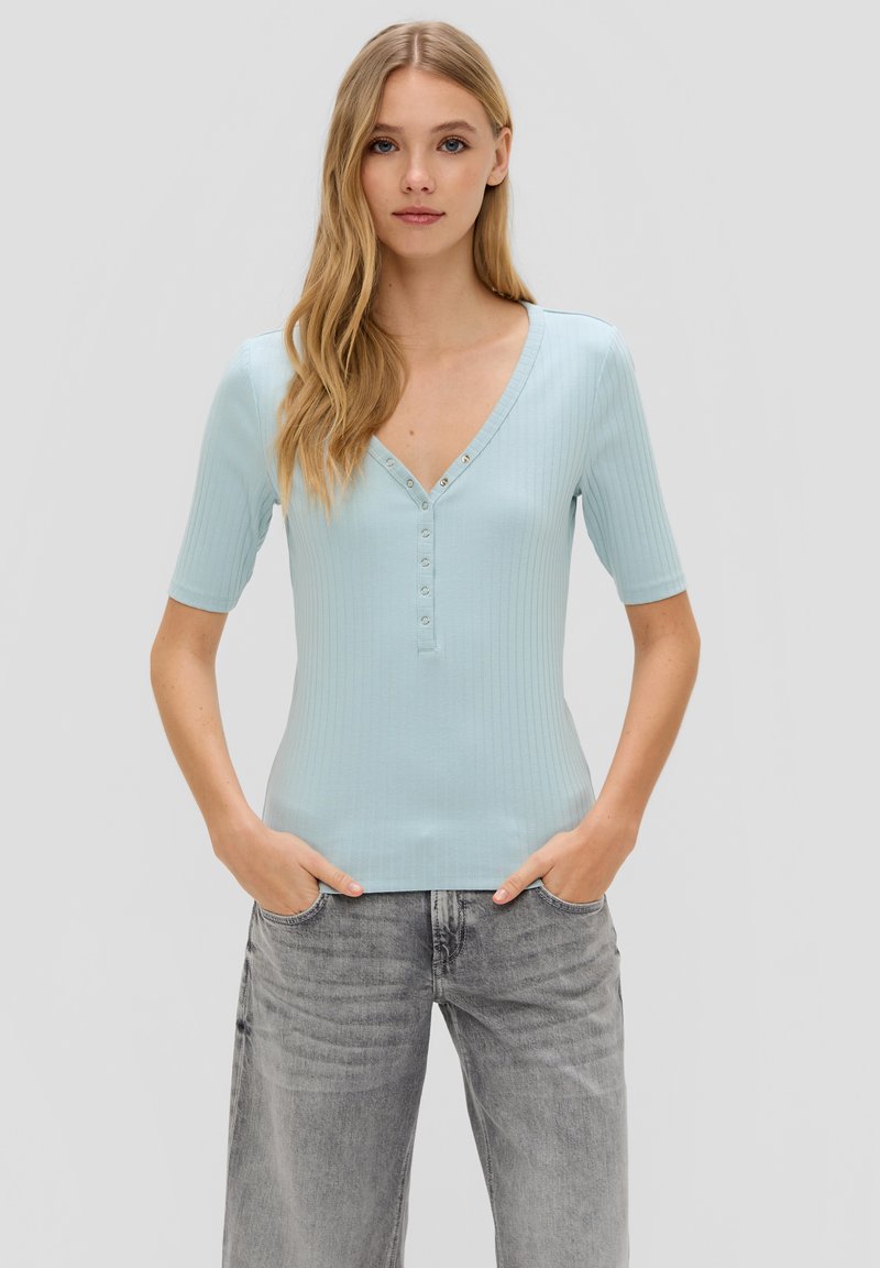 Lichtblauw geribbeld shirt met korte mouwen, v-hals en knoopdetail aan de voorkant. Gepaard met grijze wijde jeans.