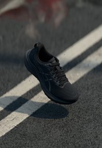 Black running shoe with a textured mesh upper, lace-up design, and a cushioned sole, featuring subtle branding and a pull tab.
