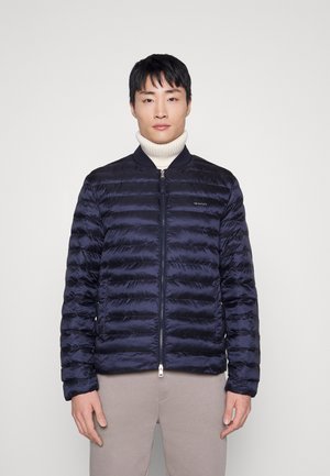 Navy puffer jacket, quilted design, lightweight material, featuring a zip front, ribbed collar, and subtle logo detail on the chest.